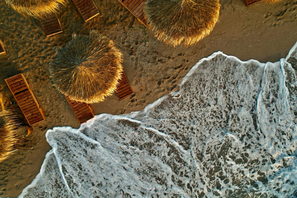 Drone shot of tropical beach with umbrellas, showcasing waves and sandy shore.