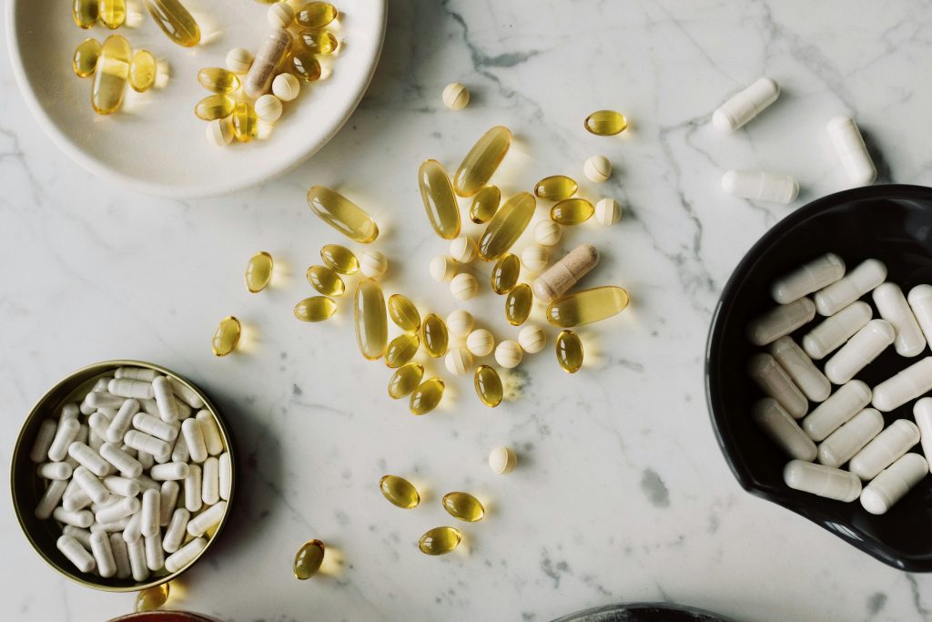 Top view of pills and capsules in gelatin shells of different sizes placed on table and various tableware in clinic