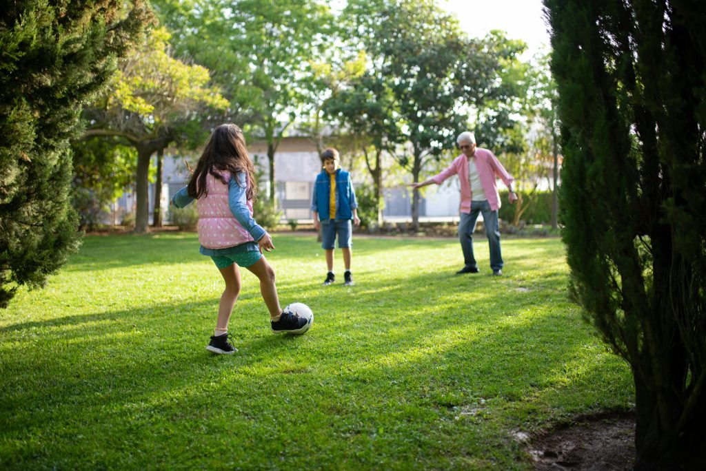 A grandfather playing football with his grandchildren in a sunny park, enjoying quality time outdoors.